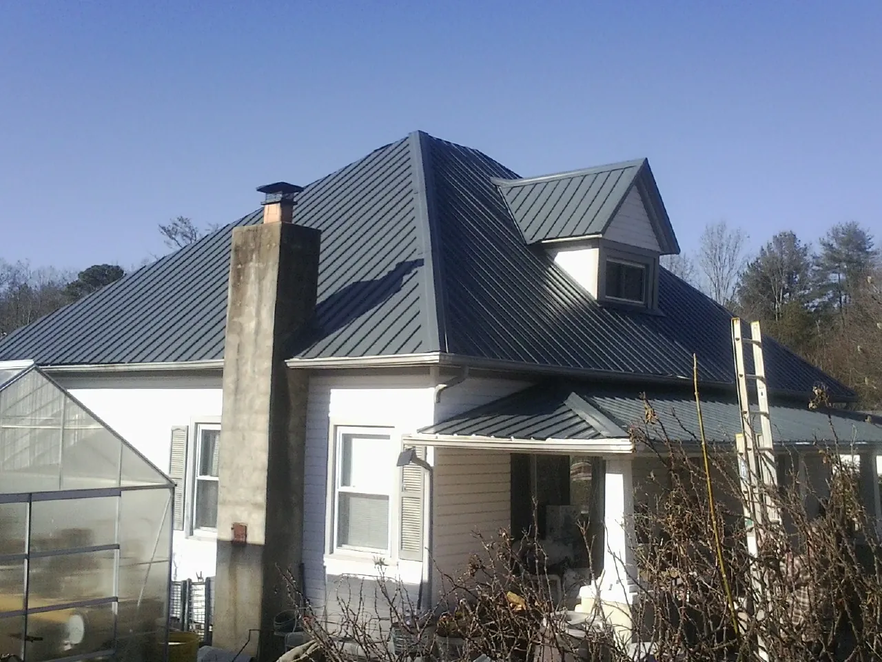 Dark blue standing seam metal roof on a white farmhouse with dormer — Slate & Tile Roof Repair by Roofing Brothers in Maple Lake