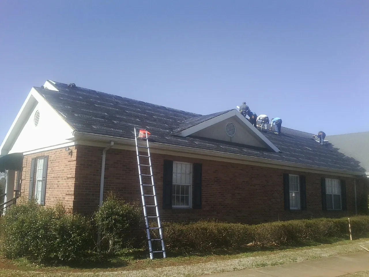 Crew tearing shingles off a brick ranch roof with a ladder set — Emergency Roof Repair work by our crew in Maple Lake