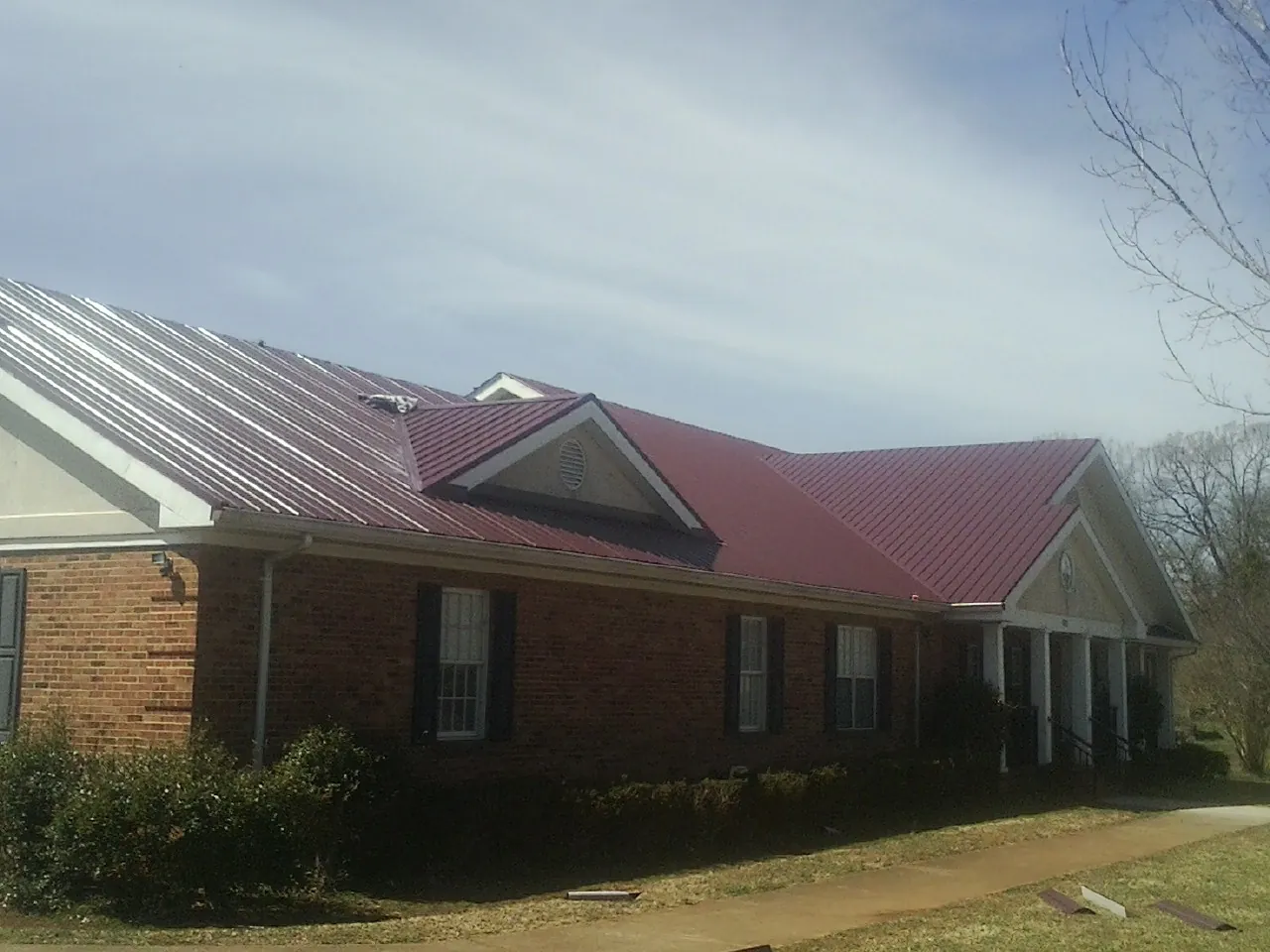 Red metal roof with gabled entries on a long brick building, from a Hail Damage Roof Repair job in Maple Lake
