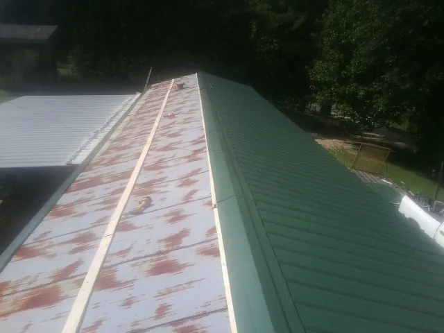 Old rusted panels beside newly installed green metal roofing — Wind Damage Roof Repair by Roofing Brothers in Maple Lake