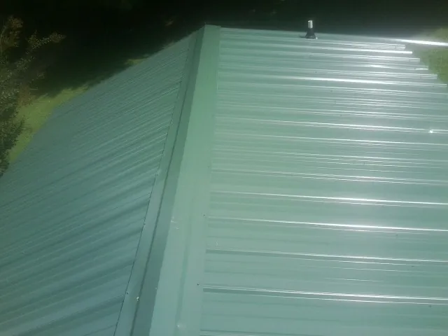 New green metal panels meeting at the ridge of a roof — Flat Roof Repair work by our crew in Maple Lake