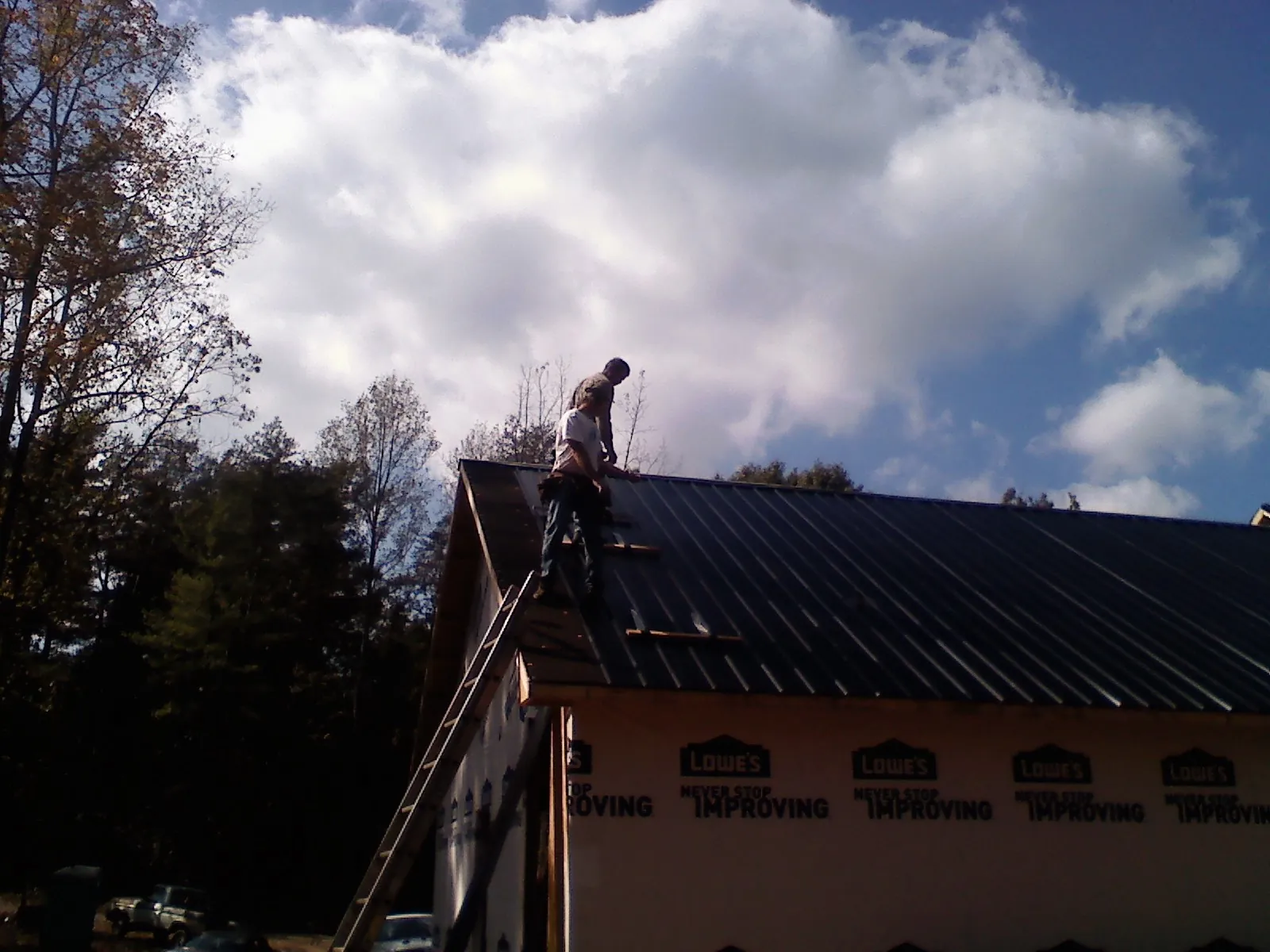 Roofer fastening dark metal panels high against a cloudy sky, from a Roof Inspection job in Maple Lake