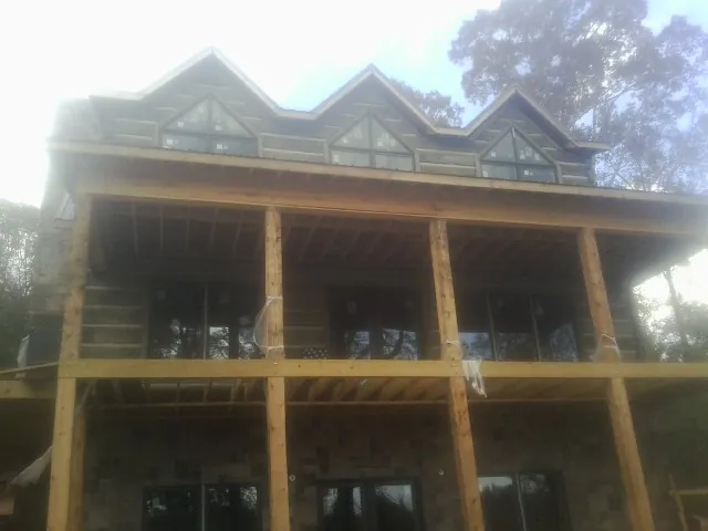 Dormers and porch framing on a large log home under construction — Roof Coating work by our crew in Maple Lake